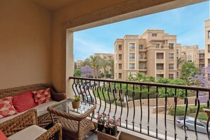 A balcony with wicker furniture, a glass table, and potted plants. - SODIC Kattameya Plaza, 3-Bedroom, 230 m² Family Apartment, 3 Pools in New Cairo (New Cairo)