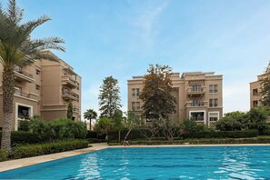 A residential building with a swimming pool, surrounded by greenery and palm trees. - SODIC Kattameya Plaza, 3-Bedroom, 230 m² Family Apartment, 3 Pools in New Cairo (New Cairo)