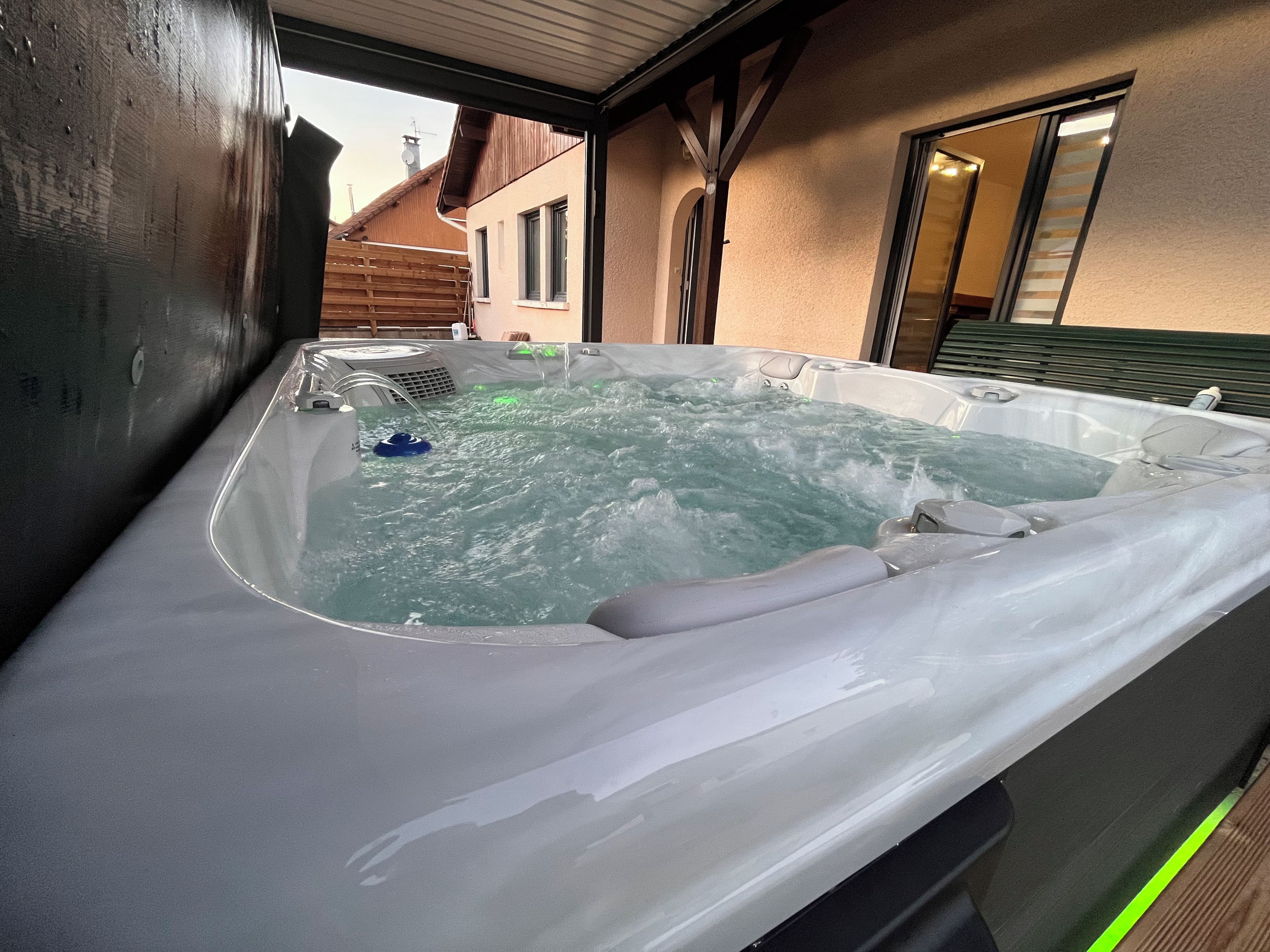Un jacuzzi con terraza de madera y una casa al fondo.