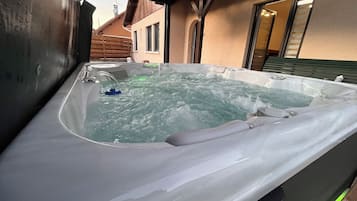 Un jacuzzi con terraza de madera y una casa al fondo.