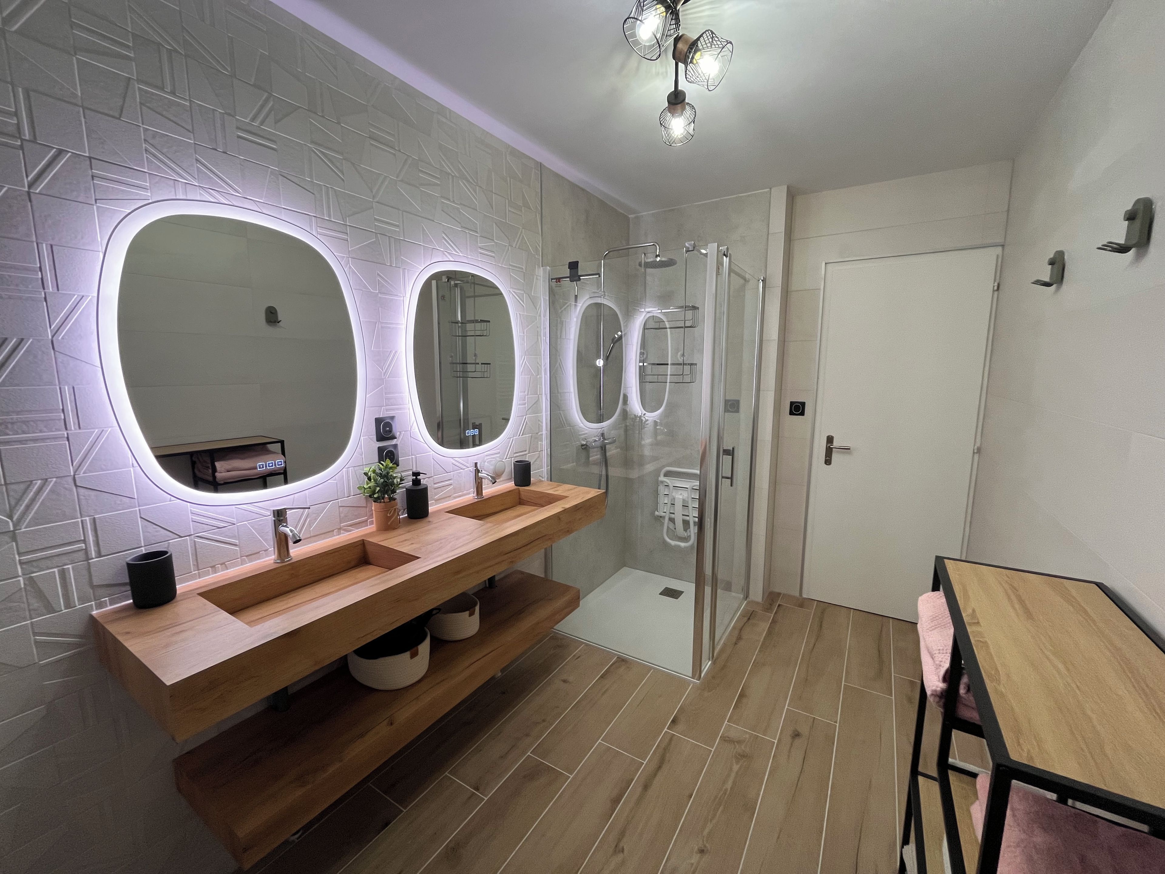 A modern bathroom with a wooden vanity, three oval mirrors, and a glass shower enclosure.