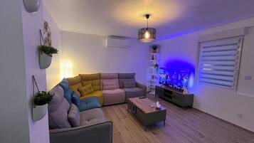 A living room with a sectional sofa, a coffee table, a TV, and decorative plants.