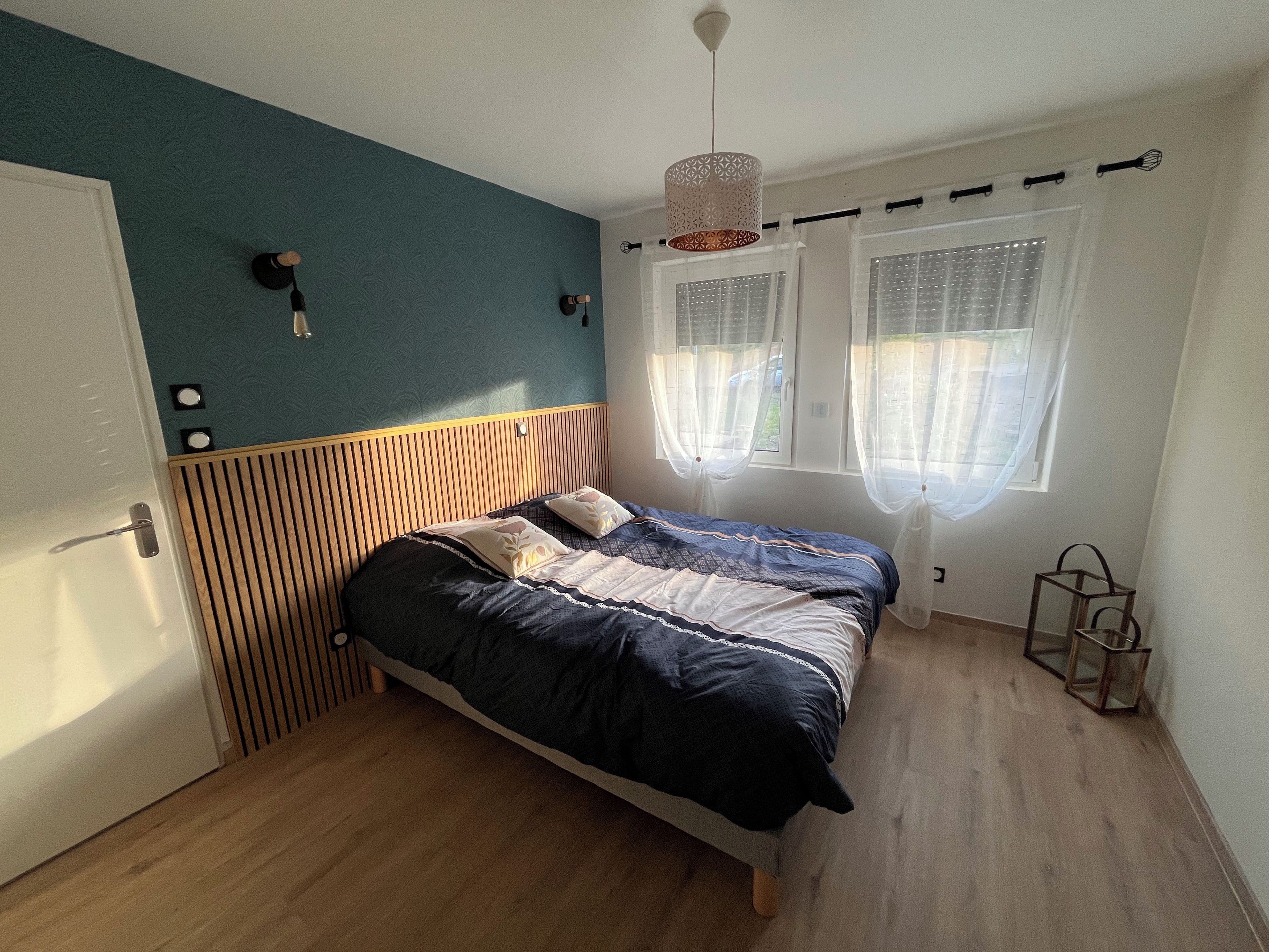 A bedroom with a bed, a door, a window with curtains, and a hanging light fixture.