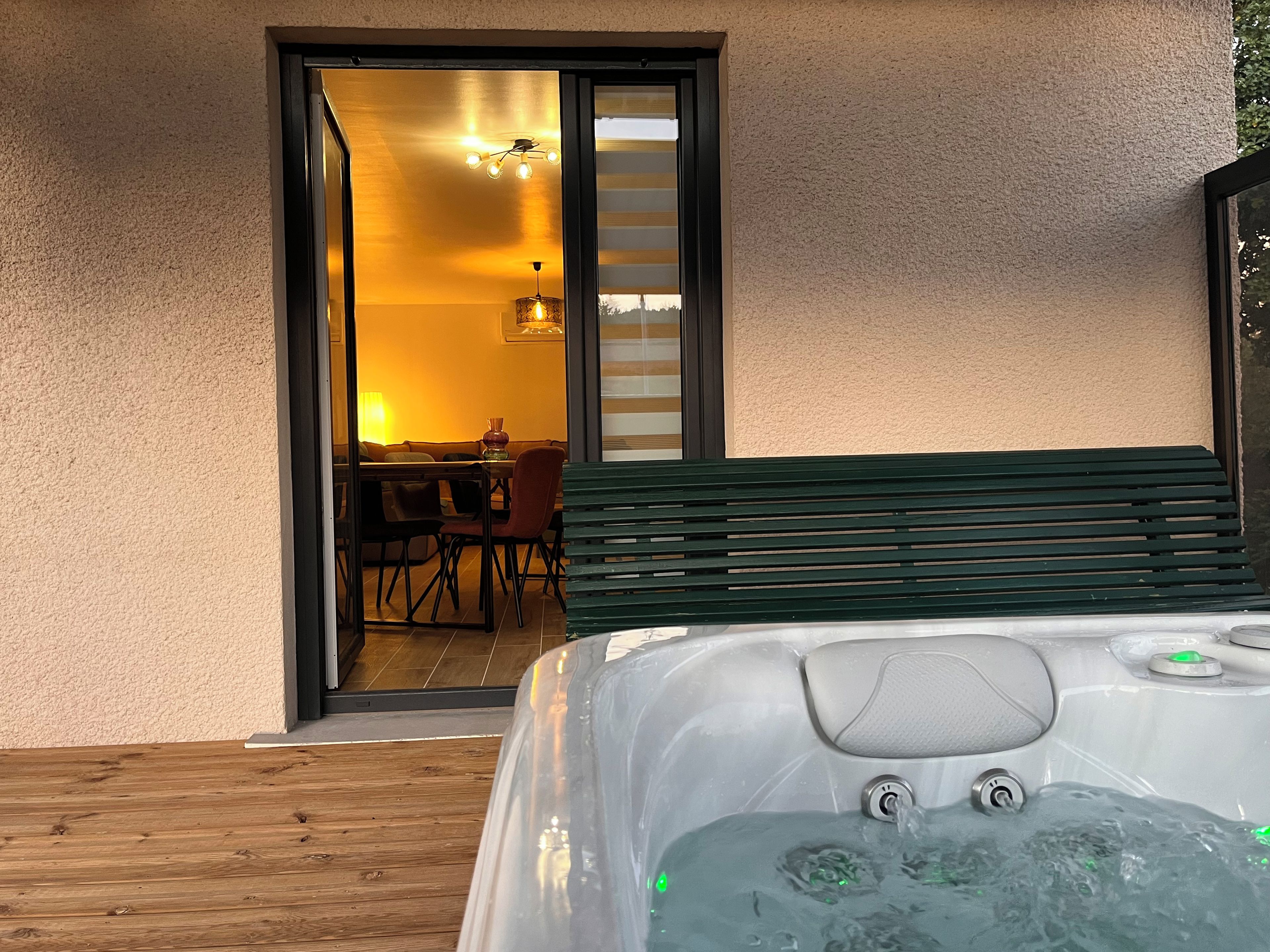 Un bain à remous sur une terrasse en bois, avec vue sur un espace repas et une porte-fenêtre coulissante.