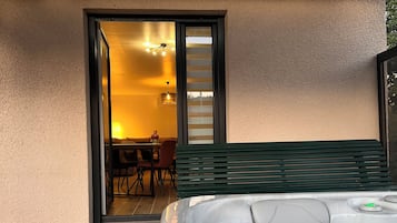 Un bain à remous sur une terrasse en bois, avec vue sur un espace repas et une porte-fenêtre coulissante.