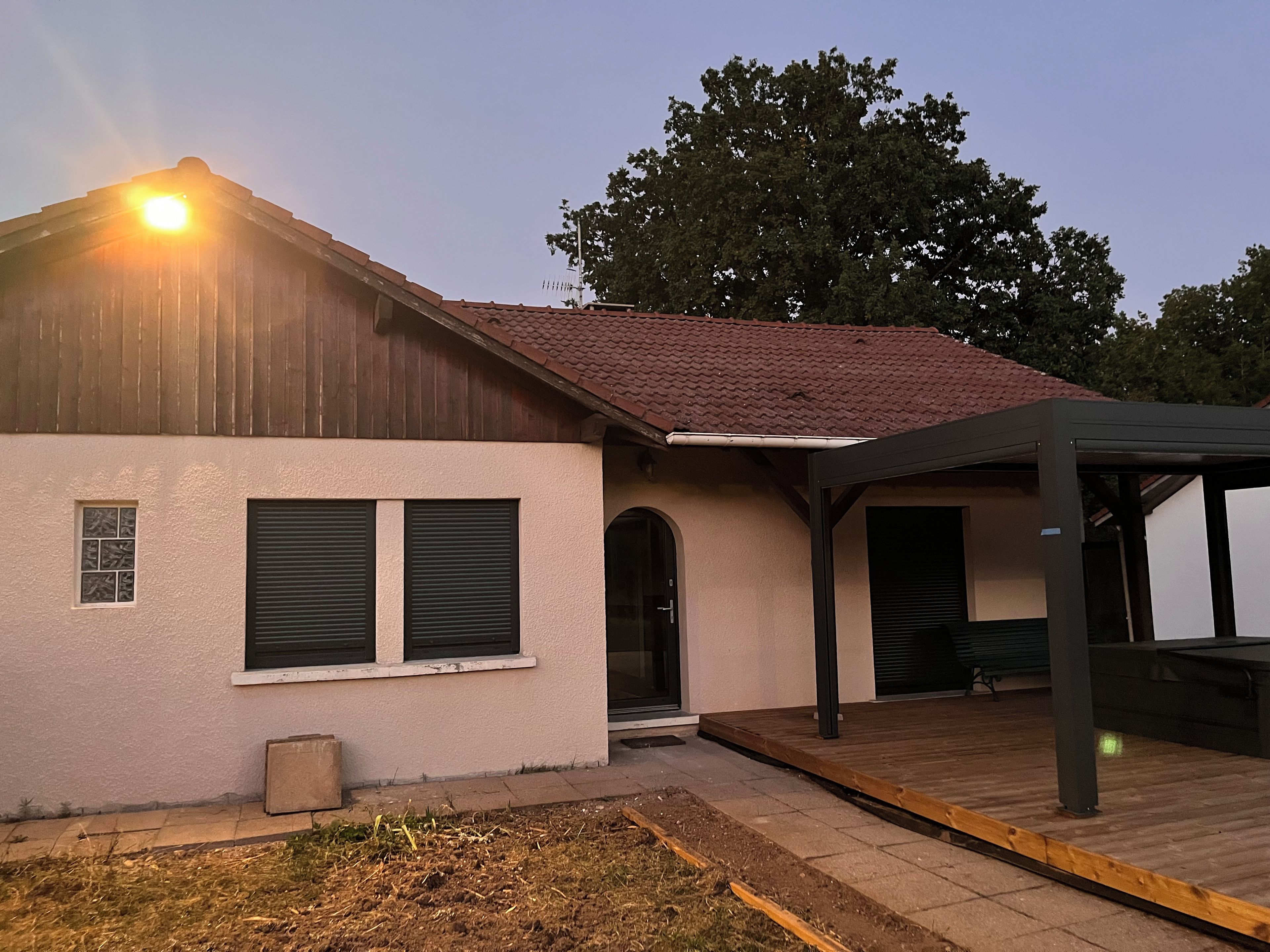 A building with a red-tiled roof, a covered porch, and a small window with shutters.