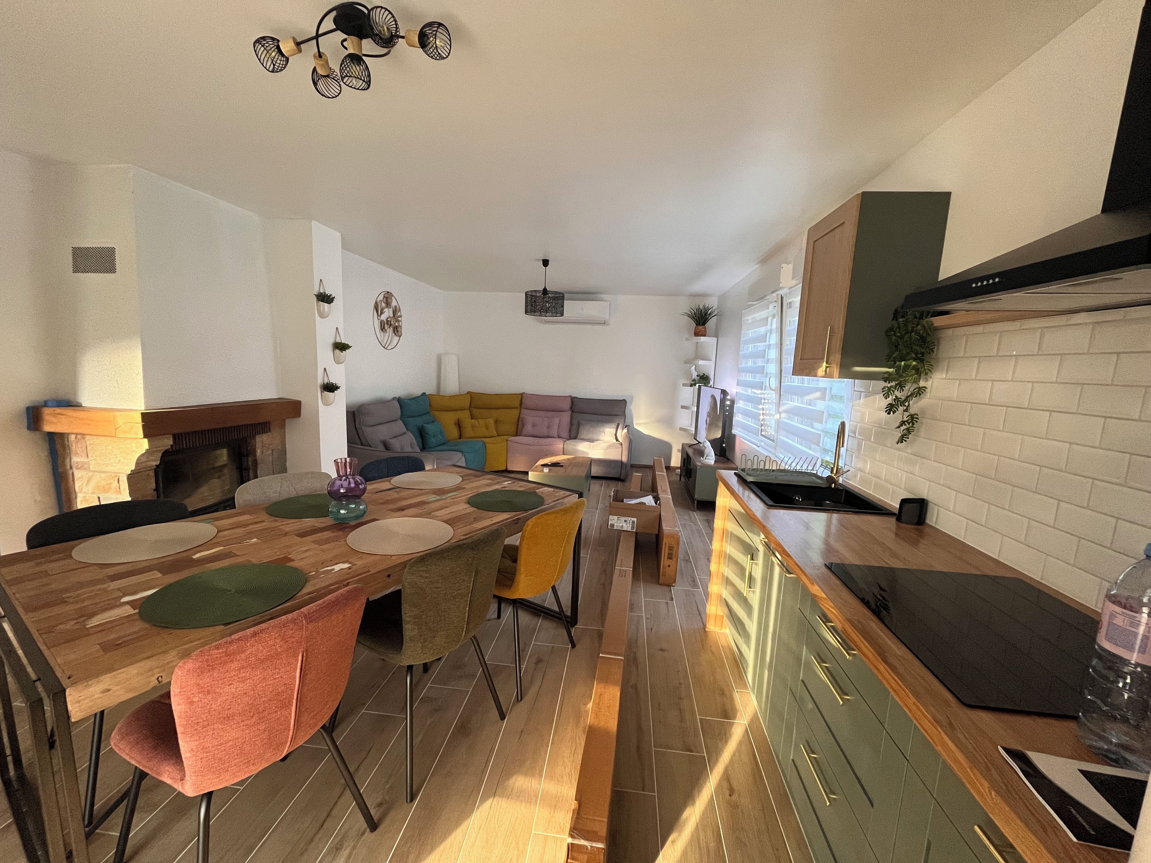 Une cuisine moderne dotée d’un four encastré, un coin repas avec une table et des chaises en bois, et un salon avec un canapé et un téléviseur.