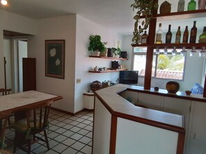Una cocina con comedor, una barra con botellas y una ventana con vista a palmeras.