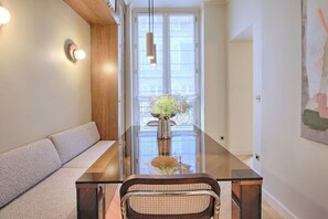 Een moderne woonkamer met een glazen eettafel, een bank en een vaas met bloemen.