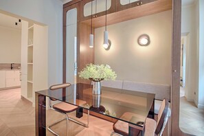 A modern dining area with a glass table, metal chairs, a vase with flowers, and pendant lighting. - Louvre Palais Royal New Luxury Flat (Paris)