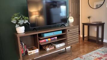 Ein Wohnzimmer mit Fernseher auf einem Holzboden, einem kleinen Tisch mit Spiegel und einem farbenfrohen Teppich auf dem Boden.