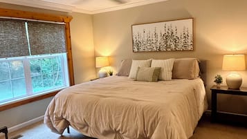 A bedroom with a bed, two bedside lamps, a ceiling fan, a window with blinds, and a wall-mounted artwork.