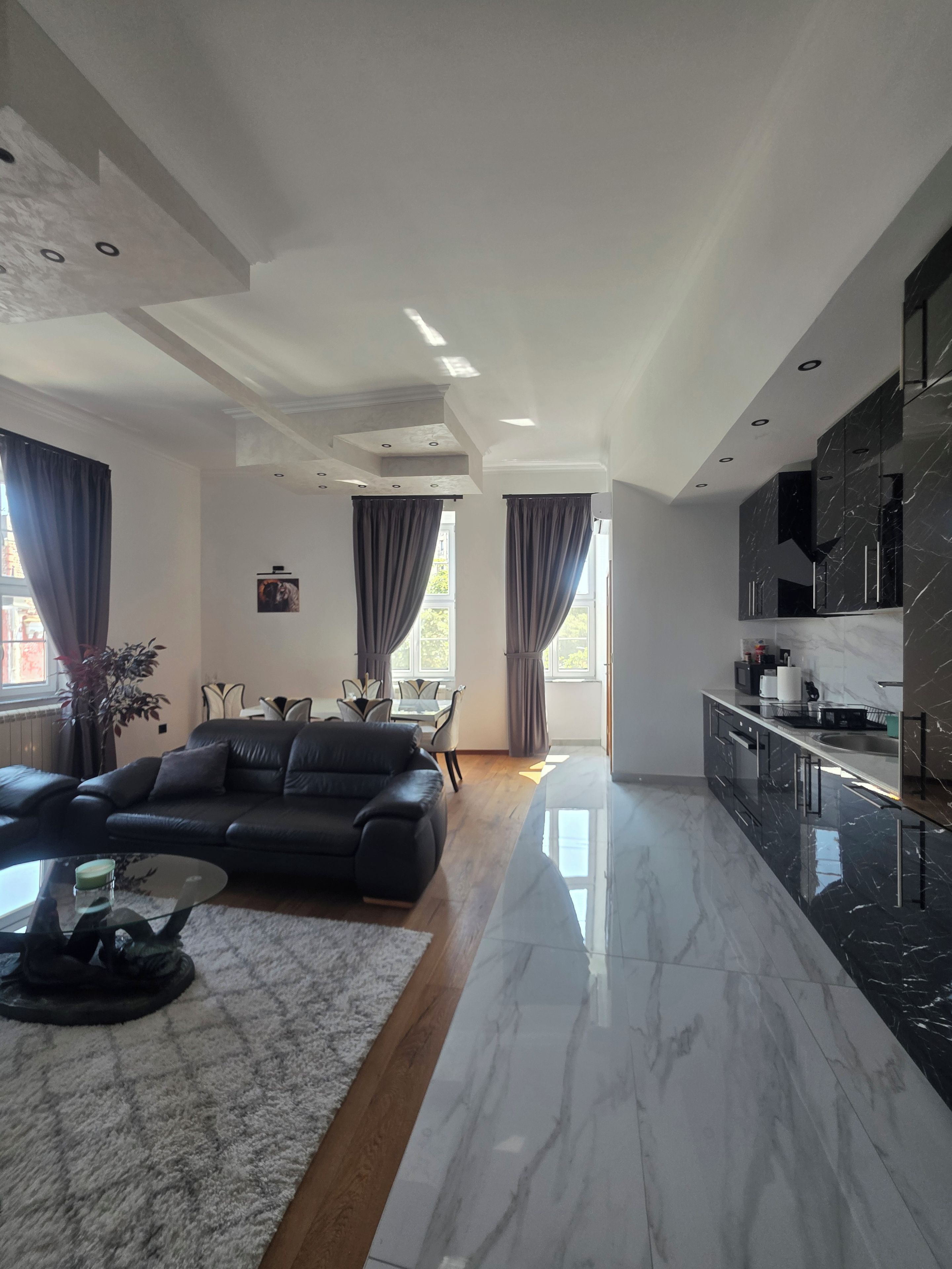 En moderne stue med en sort lædersofa, et glasbord og et spiseområde med bord og stole.