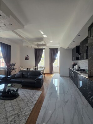 Una sala moderna con un sofá de cuero negro, una mesa de centro de vidrio y un comedor con mesa y sillas.