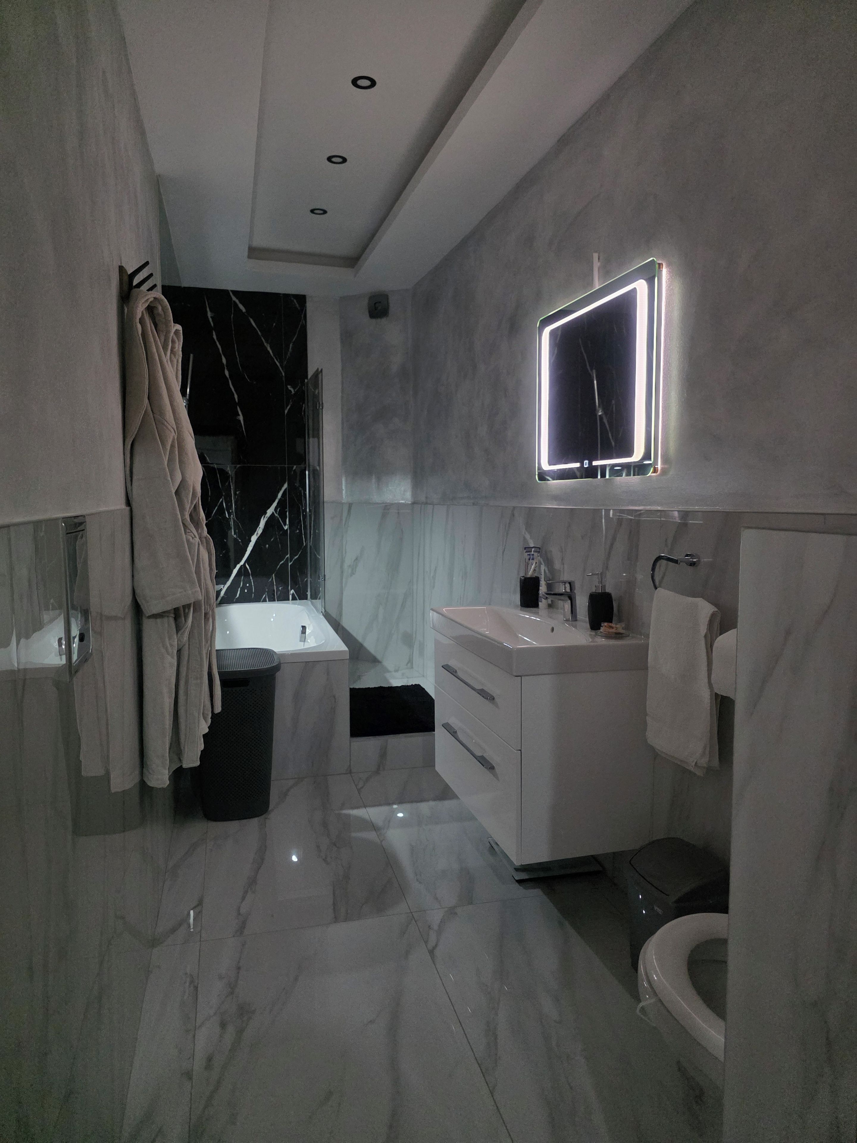 Une salle de bain moderne avec un sol en marbre, un meuble-lavabo blanc avec un miroir, une baignoire et des toilettes.
