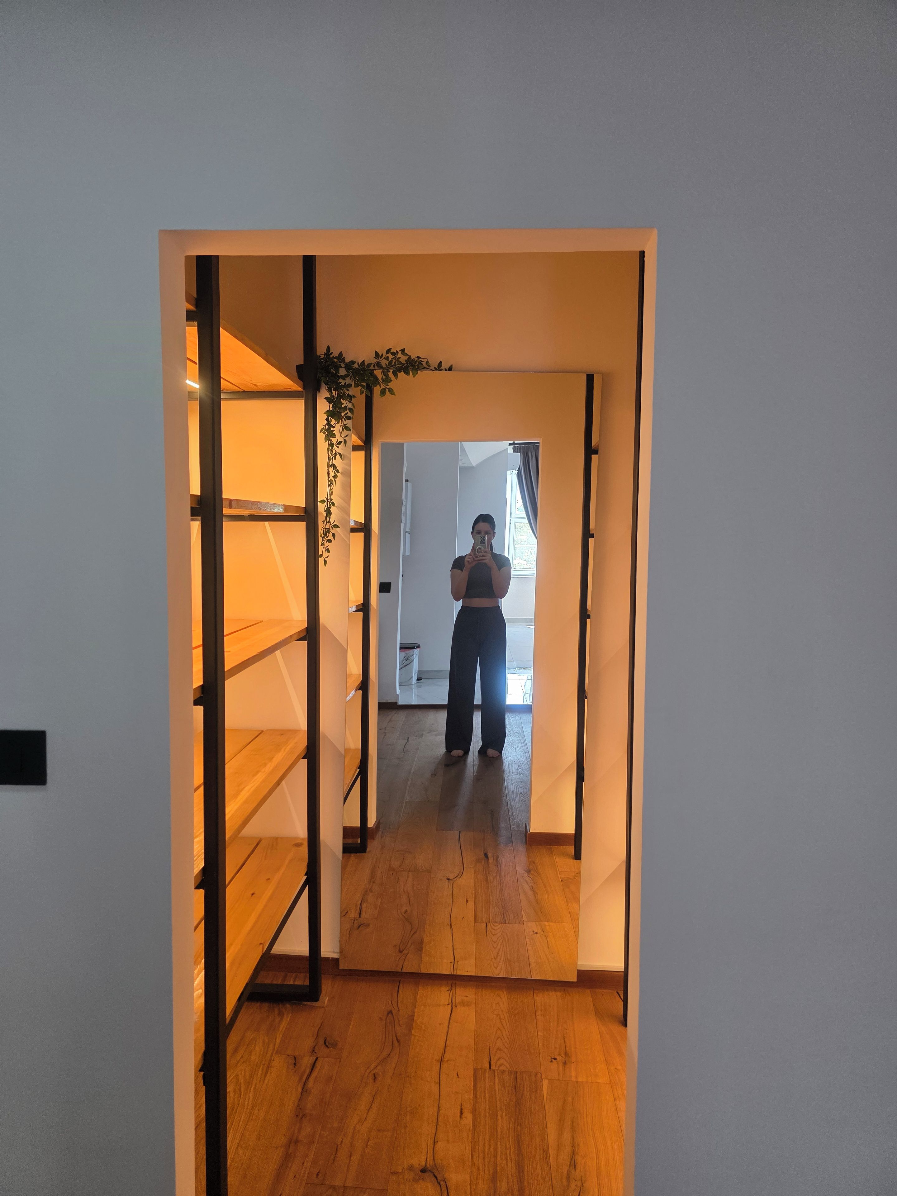 Een smalle gang met houten vloeren die leidt naar een kamer met een raam.