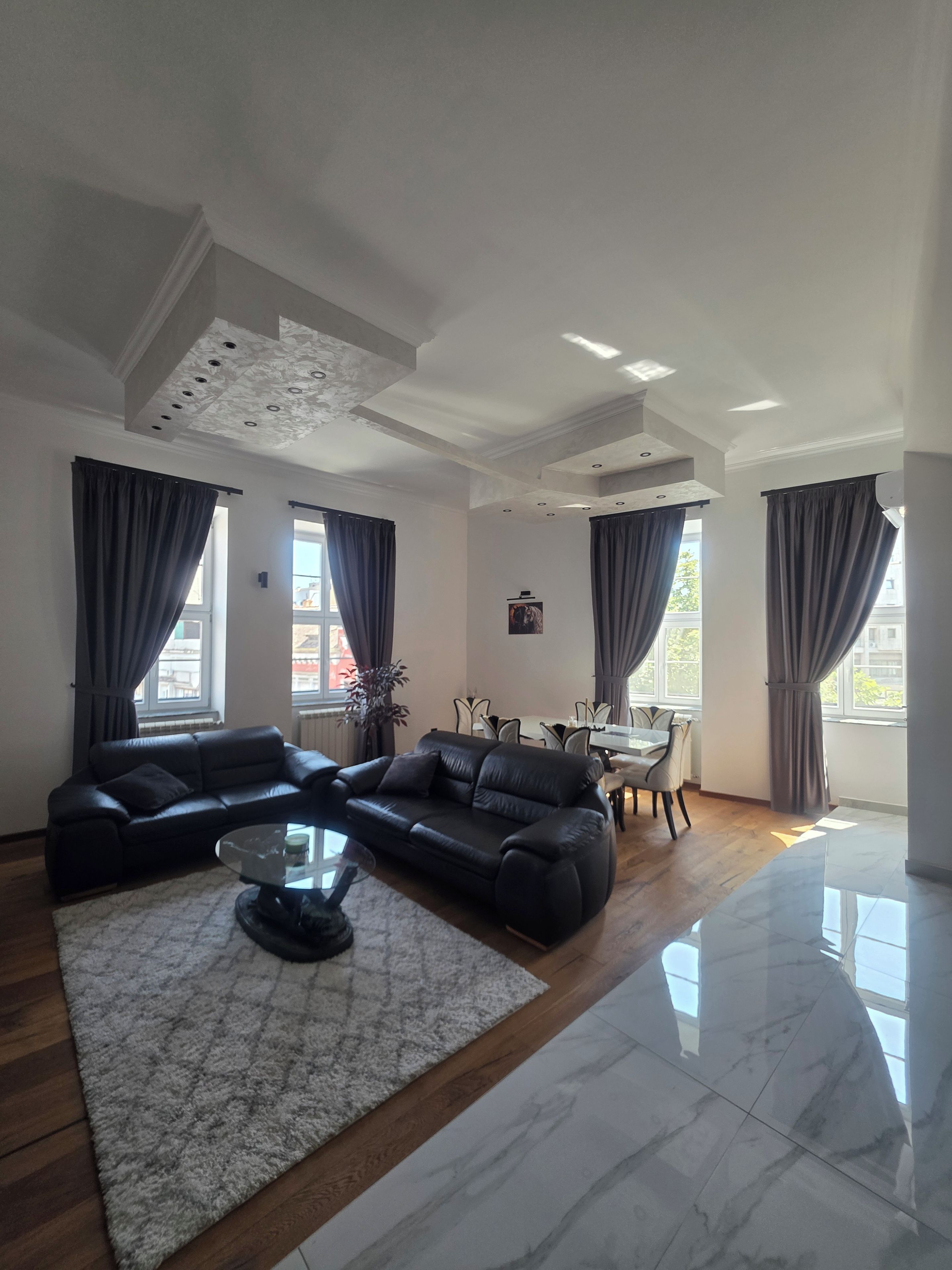 A modern living room with a sectional sofa, a glass coffee table, and a dining area with a table and chairs.