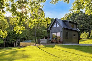 Et moderne hus med en stor glasdør, omgivet af en velplejet græsplæne og træer.