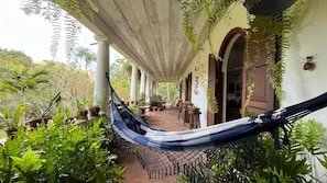 A hammock under a covered patio with potted plants and a view of the surrounding greenery. - Sítio Duncan (Teresópolis)