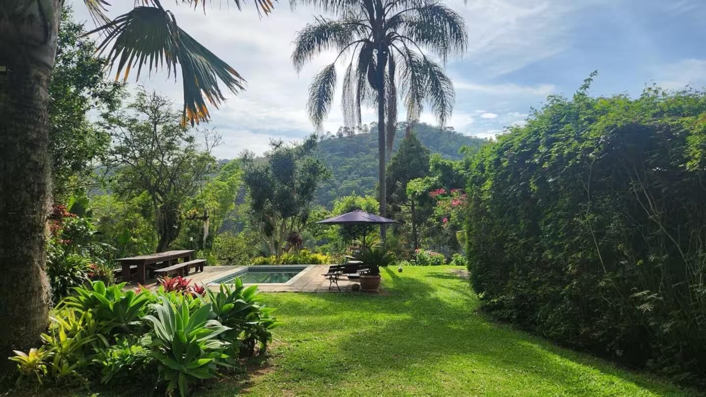 A lush garden with a pool, picnic tables, and a shaded area.