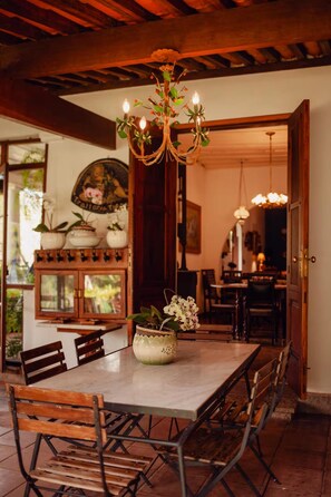 A dining area with a wooden table, chairs, a chandelier, and a potted orchid. - Sítio Duncan (Teresópolis)