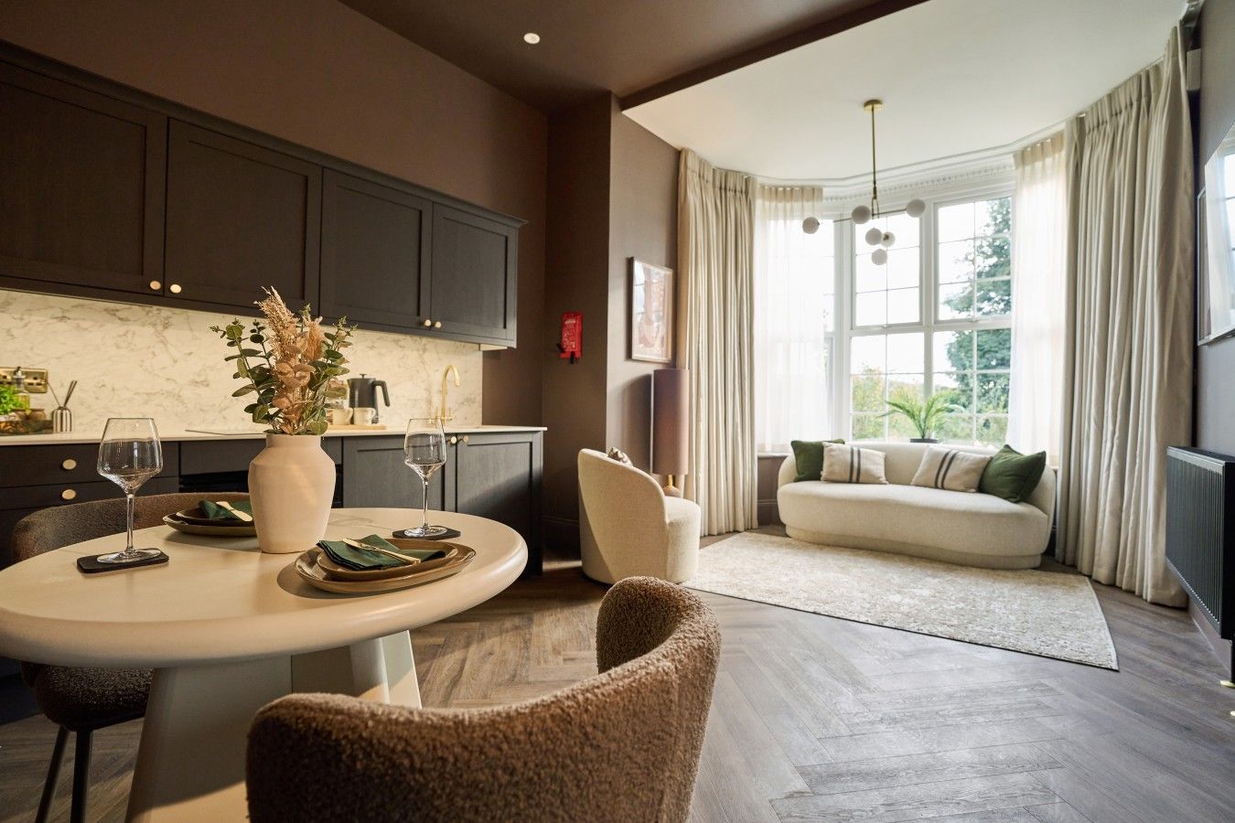 A modern kitchen with dark cabinets, a marble countertop, and a dining area with a round table and chairs.