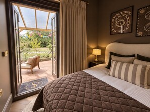 Een slaapkamer met een bed, nachtkastje, lamp en uitzicht op een tuin door een open deur.