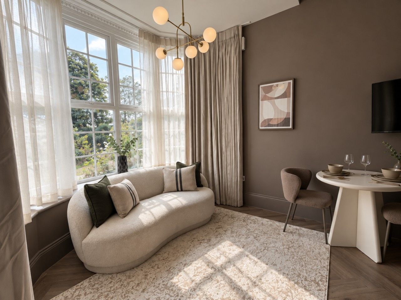 Un salon moderne avec un canapé aux lignes courbes, une table à manger et une grande fenêtre agrémentée de rideaux.