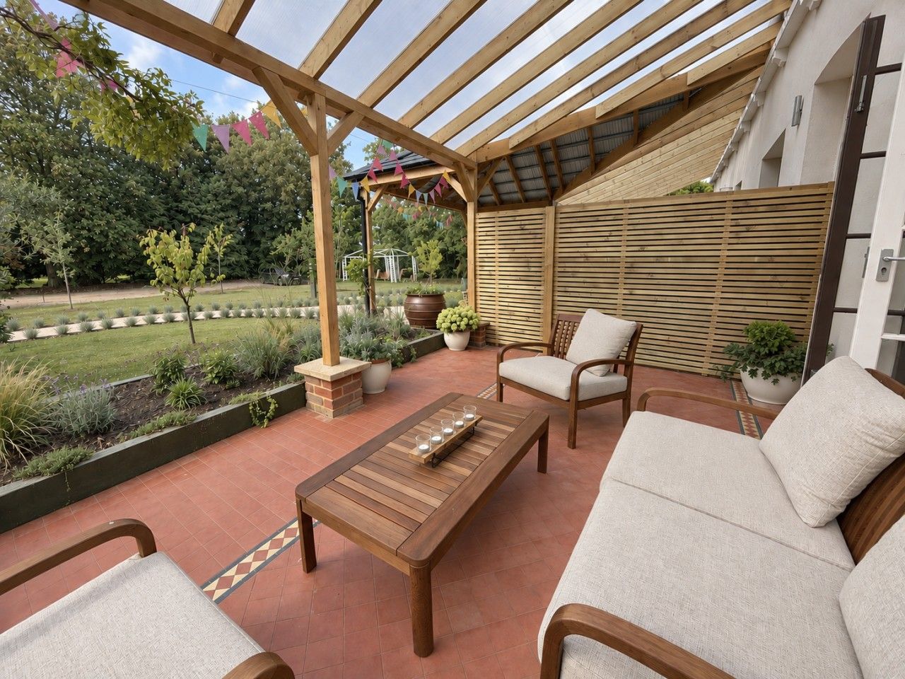 An outdoor patio with wooden furniture, a pergola, and a view of a garden.
