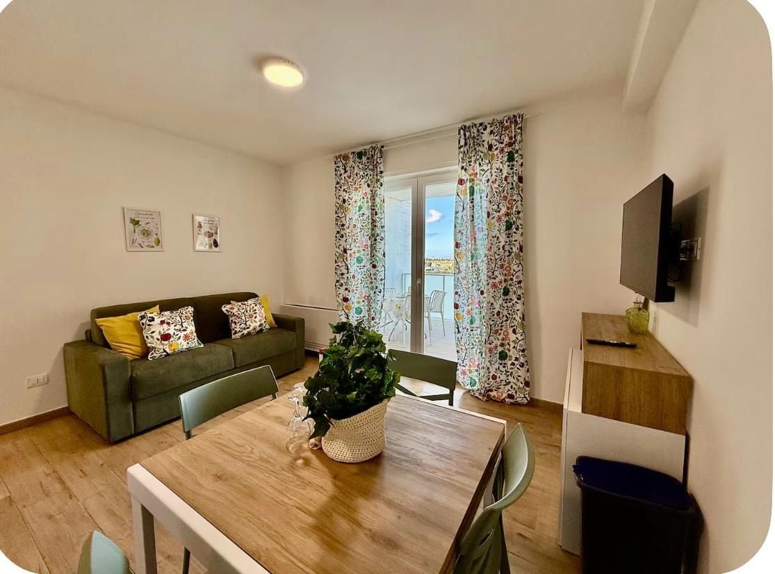 Un salon avec un canapé, une table à manger entourée de chaises, une plante en pot et un téléviseur posé sur un meuble.