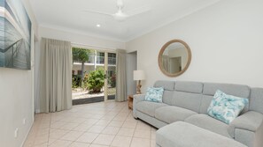 A living room with a grey sofa, a round mirror, and a view of a balcony with plants.