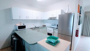 Una cocina moderna con armarios blancos, un refrigerador de acero inoxidable, un microondas y una estufa.