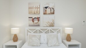 A bedroom with a white bed, two nightstands with lamps, and four wall-mounted pictures.