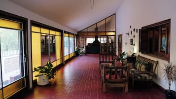 A corridor with sliding glass doors leading to a balcony, a wooden bench, and a table with chairs.