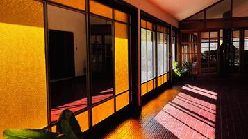 A hallway with a patterned floor, large windows with a warm glow, and a potted plant.