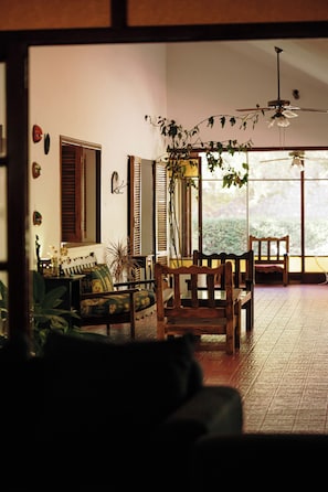 A room with a sofa, a wooden chair, a dining table, and a ceiling fan.