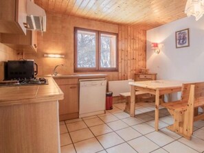 A compact kitchen with wooden cabinets, a sink, a stove, and a dining table with chairs. - Apartment 'Le Bouvreuil Ouille Du Midi' with Mountain View (Bonneval-sur-Arc)