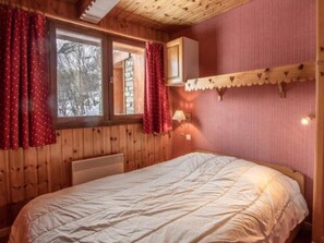 A bedroom with a wooden ceiling, a bed with a white duvet, a window with red curtains, and a wall-mounted shelf with a lamp. - Apartment 'Le Bouvreuil Ouille Du Midi' with Mountain View (Bonneval-sur-Arc)