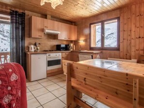 A wooden cabin interior with a kitchen, dining table, and a view of snow-covered mountains. - Apartment 'Le Bouvreuil Ouille Du Midi' with Mountain View (Bonneval-sur-Arc)
