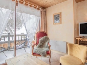 A cozy room with a red chair, a yellow armchair, a wooden table, a television, and a view of a snowy landscape through a window with sheer curtains. - Apartment 'L'Aigle Chalet Ouille Du Midi' with Mountain View (Bonneval-sur-Arc)