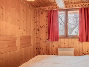 Ein Zimmer aus Holz mit einem Bett, einem Fenster mit Vorhängen und einer Heizung.