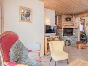 A cozy living room with a fireplace, a television, and a red upholstered chair. - Apartment 'L'Aigle Chalet Ouille Du Midi' with Mountain View (Bonneval-sur-Arc)