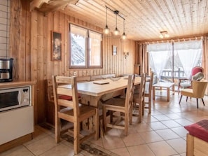 A wooden interior with a dining table, chairs, a kitchen area, and a window with curtains. - Apartment 'L'Aigle Chalet Ouille Du Midi' with Mountain View (Bonneval-sur-Arc)