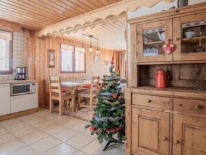 Ein Holzinterieur mit einem Esstisch, Stühlen, einer kleinen, verzierten Weihnachtstanne und einem Schrank mit Glastüren.