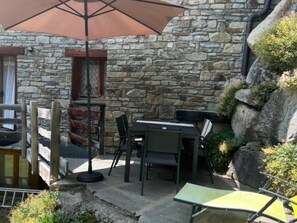 Eine Terrasse im Freien mit einer Steinmauer, einem Tisch mit Stühlen und einem großen Sonnenschirm.