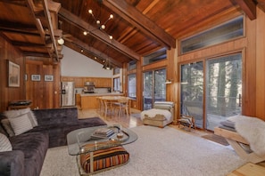 A spacious living area with a dark-colored sofa, a glass coffee table, and a fireplace. - River Hutte – Hot Tub, Pool Table & River Front (Mount Hood Village)