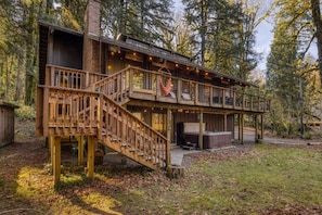 A two-story wooden cabin with a deck, a hot tub, and a fireplace. - River Hutte – Hot Tub, Pool Table & River Front (Mount Hood Village)