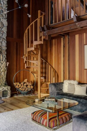 A cozy living room with a spiral staircase, a glass coffee table, a sofa, and a stone wall. - River Hutte – Hot Tub, Pool Table & River Front (Mount Hood Village)