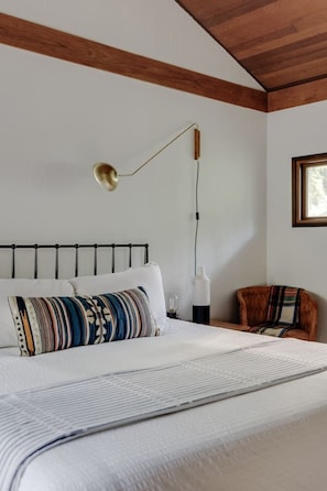 A bedroom with a bed, a bedside table, a lamp, a chair, and a window. - River Hutte – Hot Tub, Pool Table & River Front (Mount Hood Village)