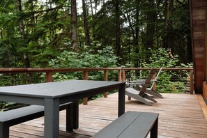 Eine Holzterrasse mit Tisch und Bänken, umgeben von einem Wald.